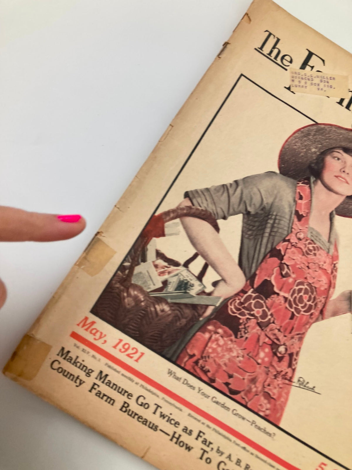 Close-up of the May 1921 issue of The Farm Journal Magazine, highlighting a woman's hand pointing at the title and articles related to farming practices and federal farm loans.