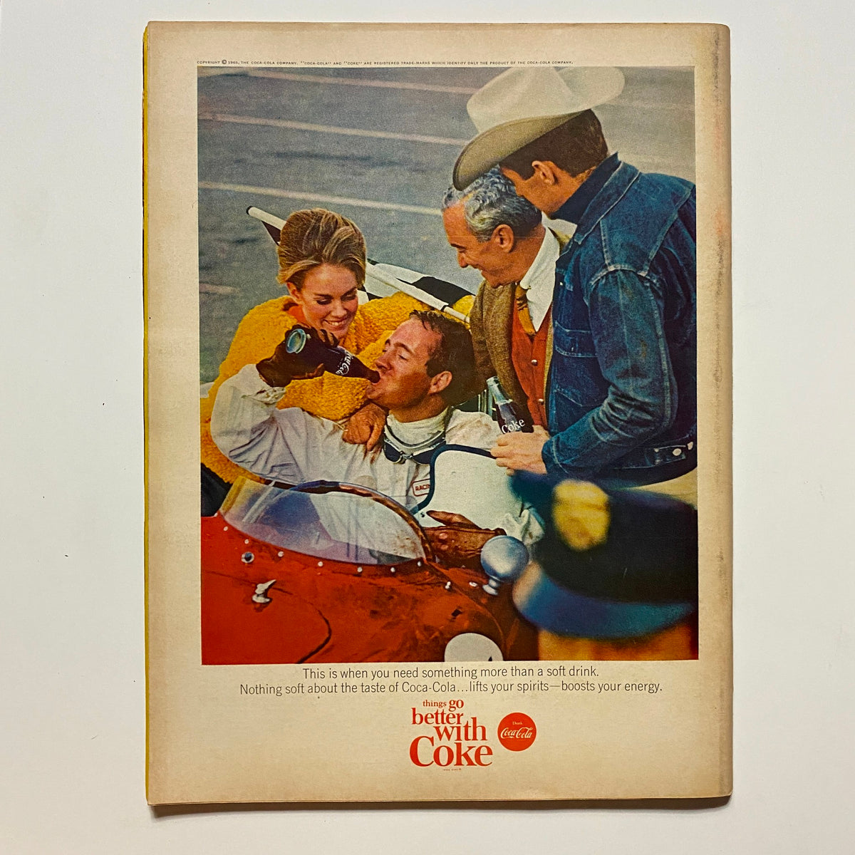 Back cover of VTG Hot Rod Magazine May 1965 displaying a Coca-Cola advertisement with a vintage scene of a racer celebrating with friends, emphasizing the social aspect of car culture.