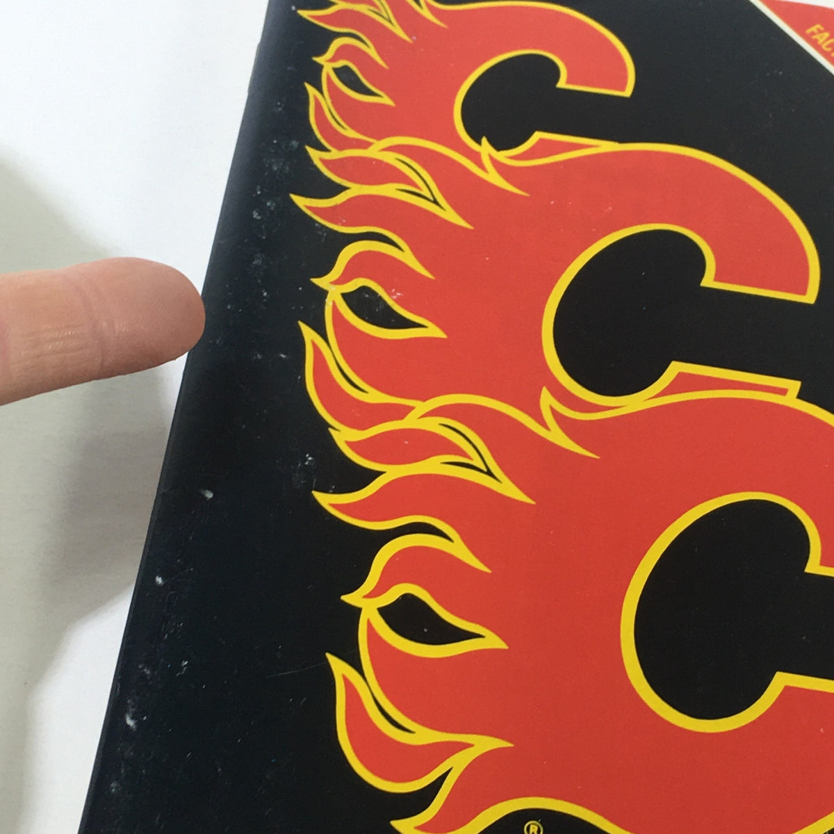 Close-up of the edge of the VTG NHL Official Fact Book 1982-1983 - Calgary Flames showing signs of wear and a finger pointing to the damaged area.