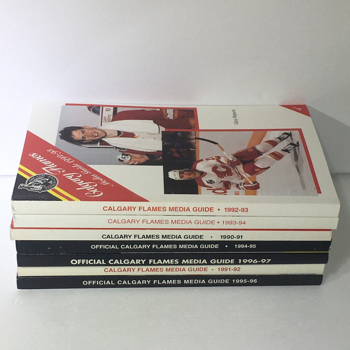 Lot of 7 VTG NHL Official Calgary Flames Media Guide 1990 - 1997 stacked together, displaying season titles and images of Calgary Flames players.