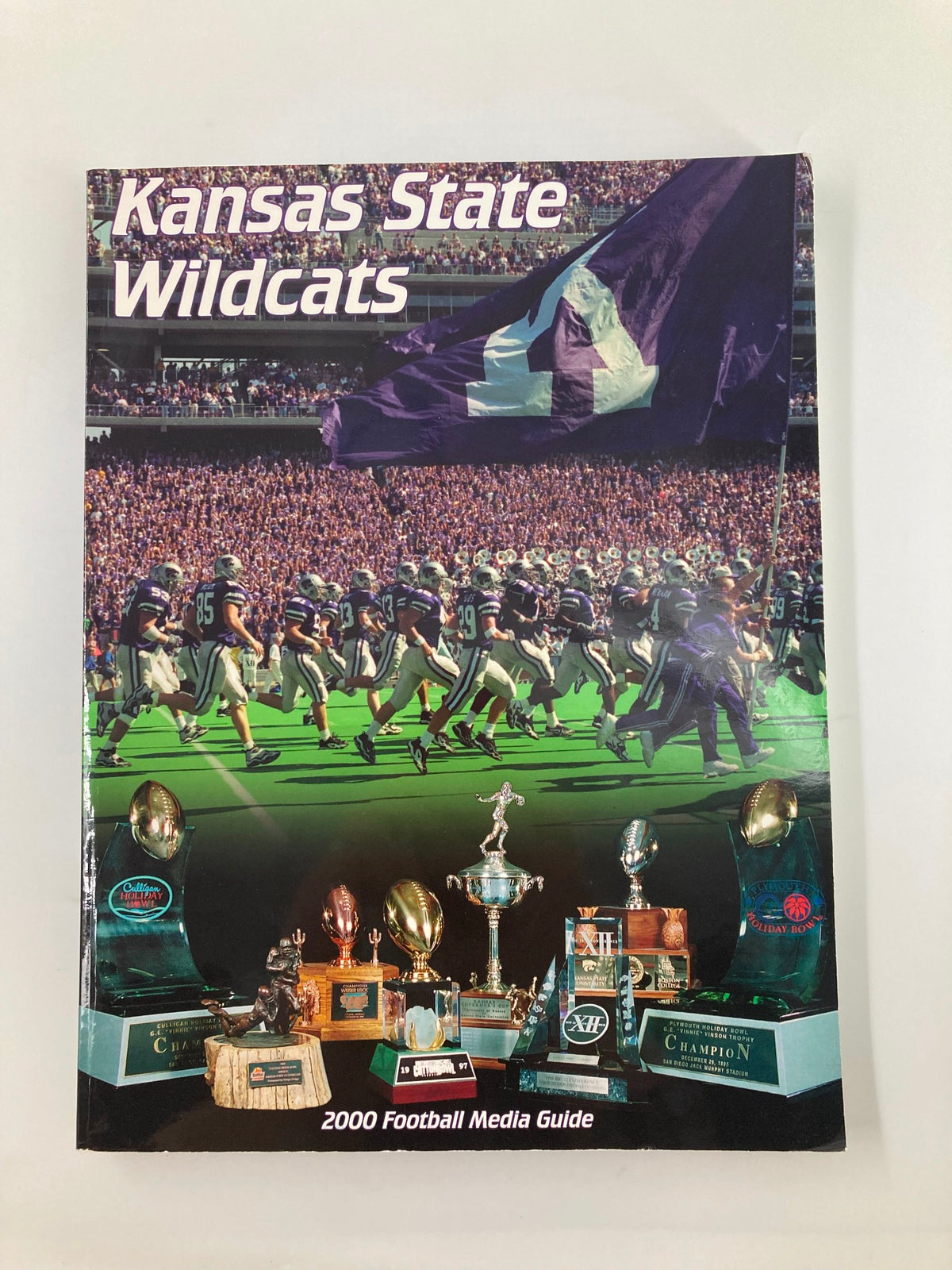 Cover of the 2000 Kansas State Wildcats Football Media Guide featuring players and a large Kansas State flag, symbolizing team spirit during the game.