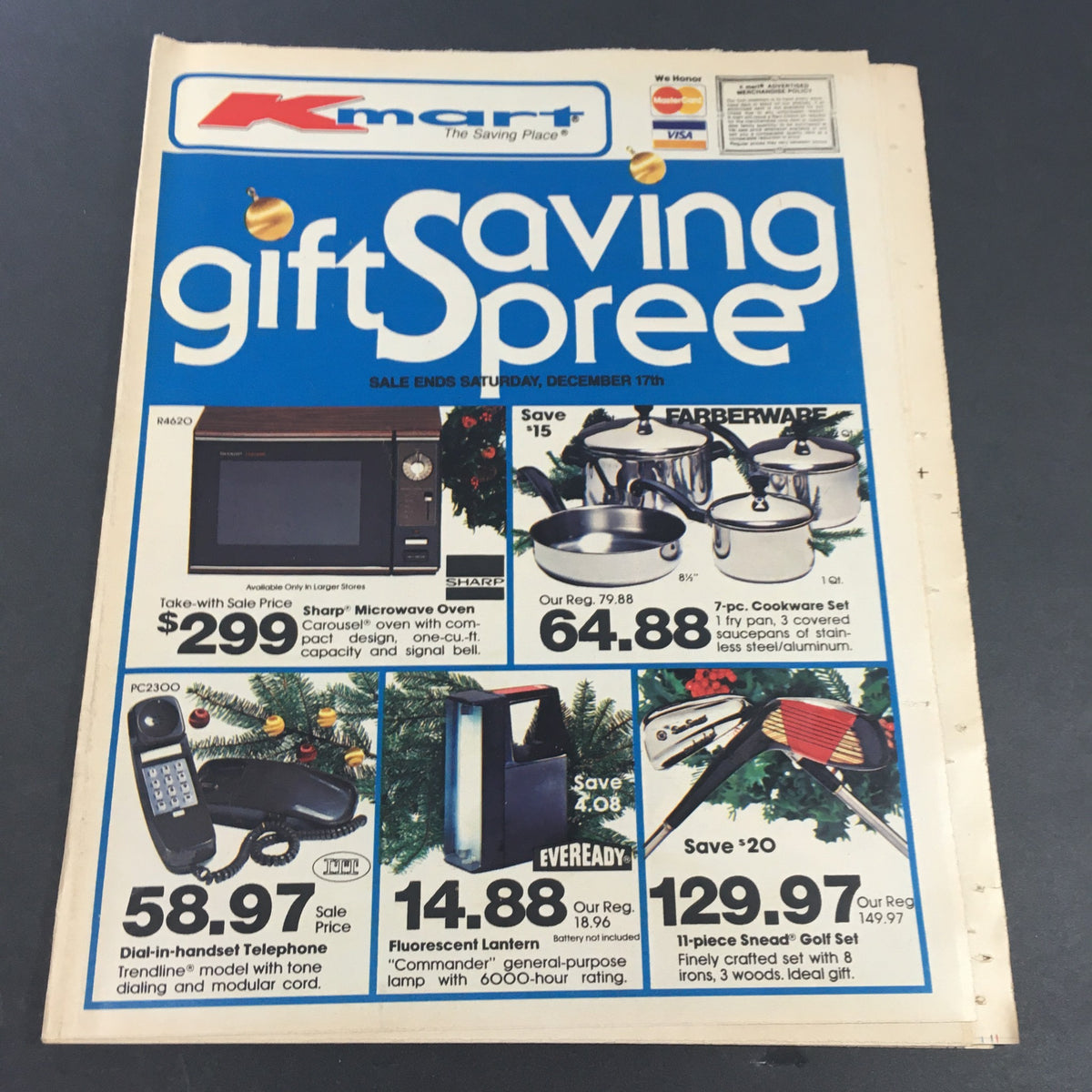 Vintage advertisement for December 1983 K-Mart Gift Saving Spree Circular featuring various holiday products, including a microwave oven, cookware set, and golf set, showcasing sale prices and promotional offers.