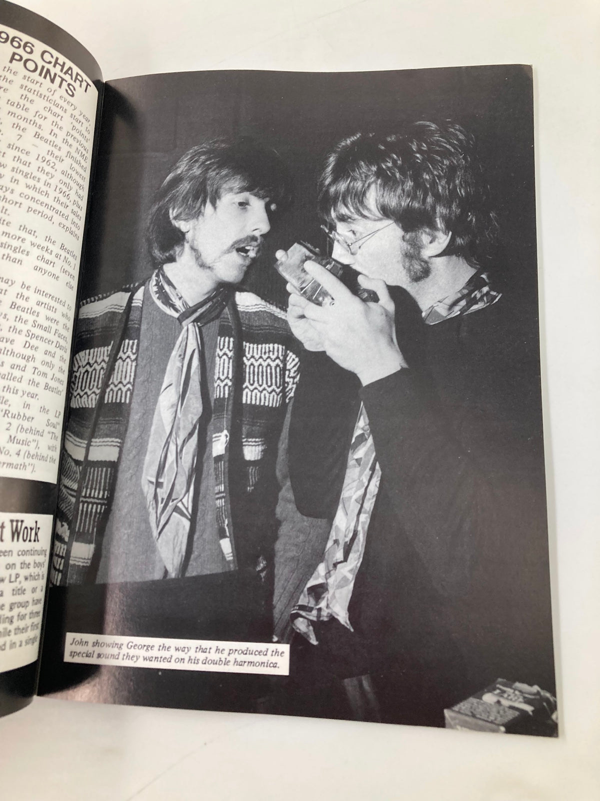Black and white image from The Beatles Book Monthly Magazine February 1987 Issue #130, showing John Lennon demonstrating a technique to George Harrison while using a double harmonica.