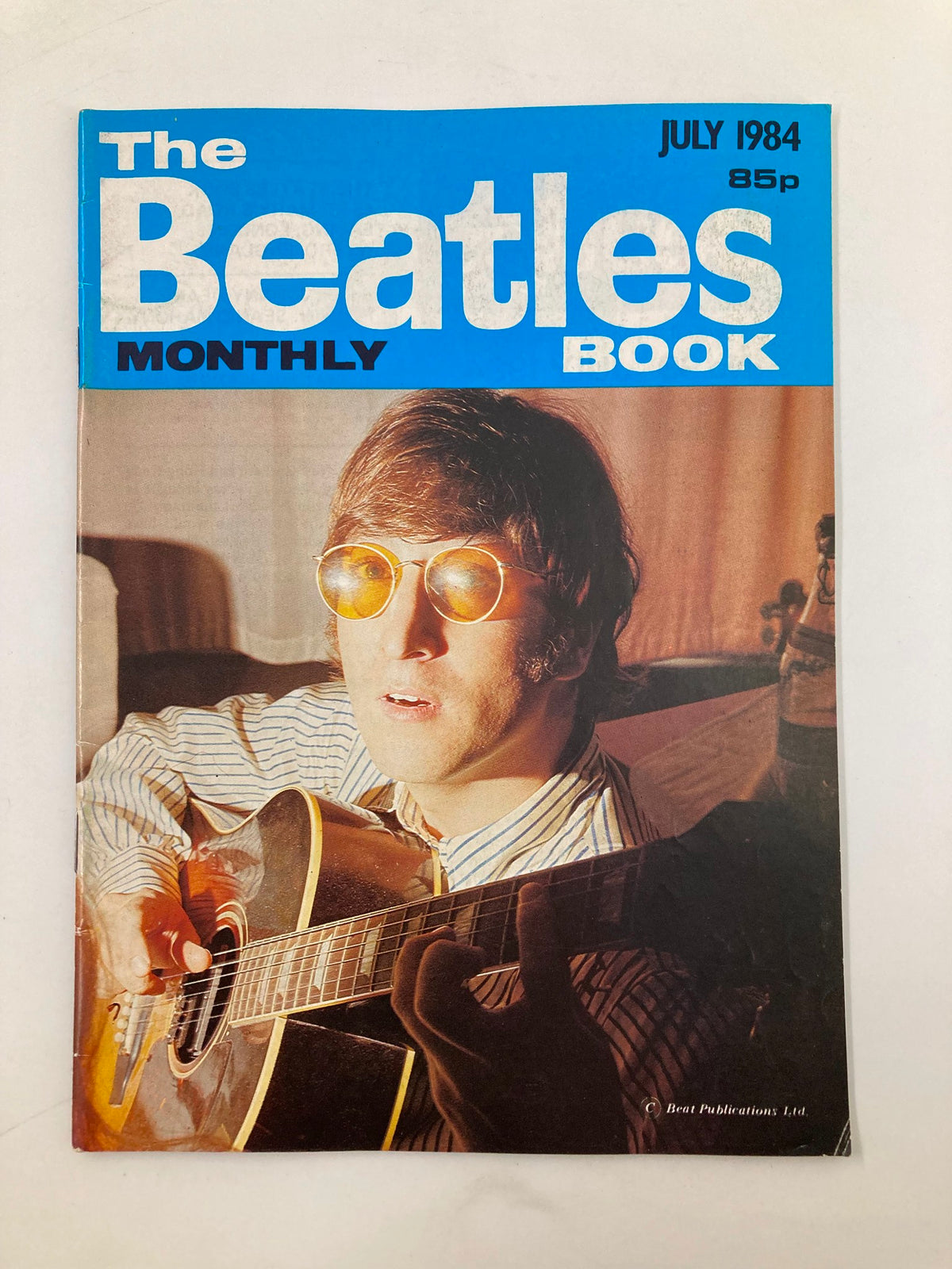 Cover of The Beatles Book Monthly Magazine July 1984 #99 featuring John Lennon wearing sunglasses and playing guitar.