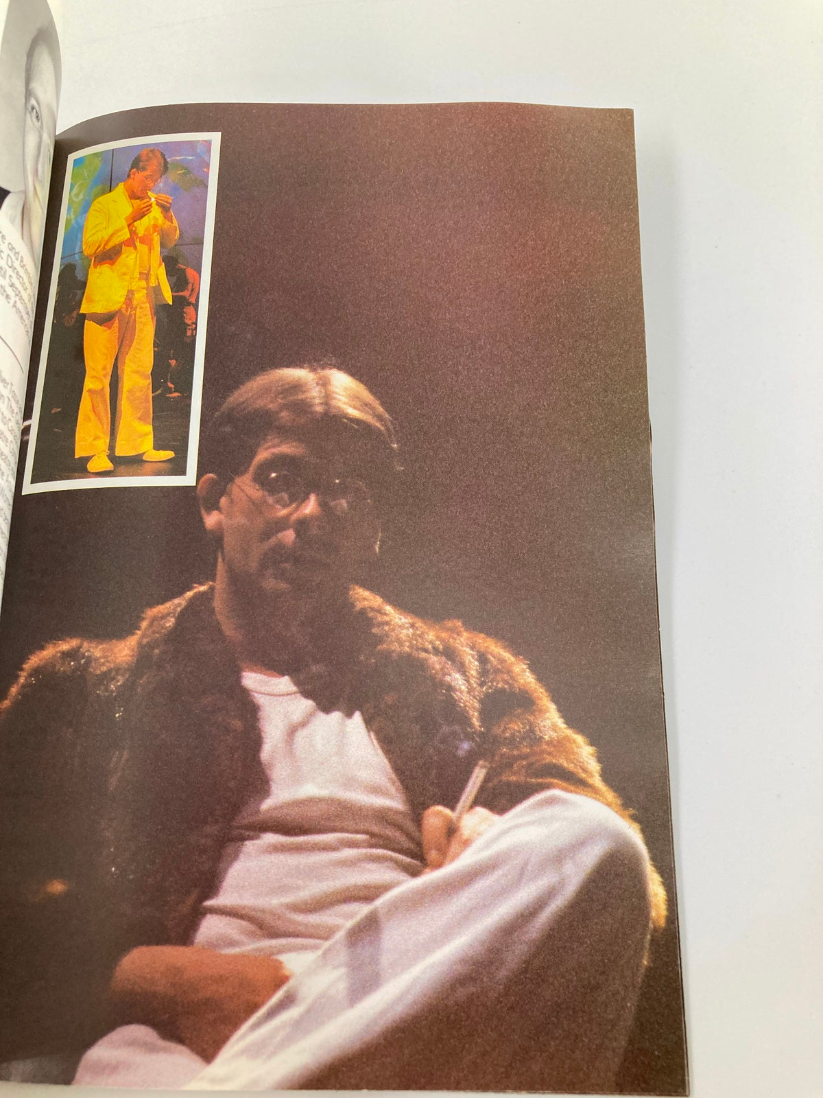 A performer dressed in a fur coat seated pensively during the 1985 John Lennon at the Astoria Theatre, captured by Bob Eaton.
