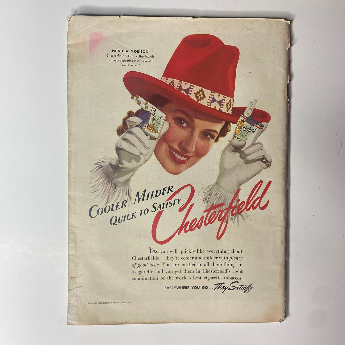 Advertisement for Chesterfield cigarettes featuring a smiling woman in a red hat and white gloves holding cigarette packs, from Time Magazine May 26, 1941 Vol 37 No. 21.