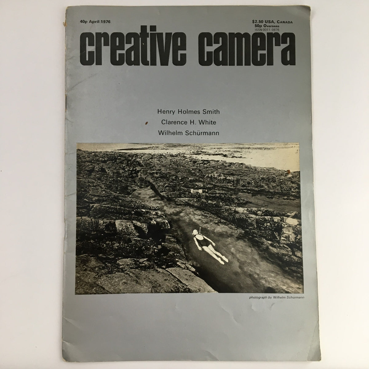 Creative Camera Magazine April 1976 cover featuring a black and white photograph by Wilhelm Schürmann, showcasing a serene landscape with a submerged figure.