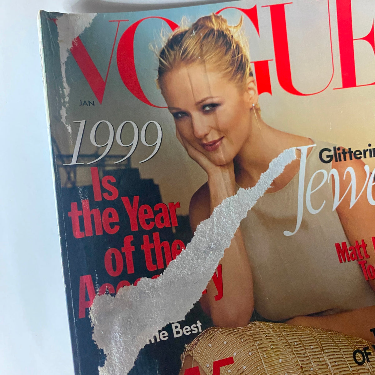 Close-up of the damaged cover of Vogue Magazine January 1999, focusing on the title 'Glittering Jewel' by Steven Meisel, highlighting the model's pose and facial expression.
