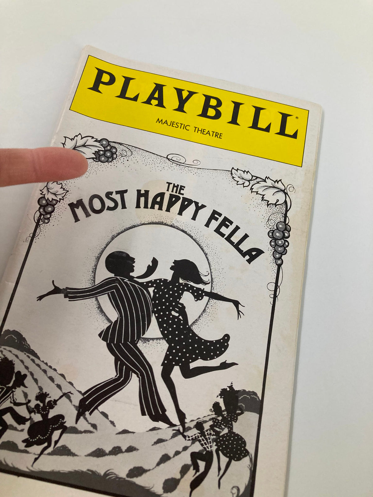 Close-up of the 1979 Playbill for The Most Happy Fella at Majestic Theatre with a hand pointing at the cover illustration.