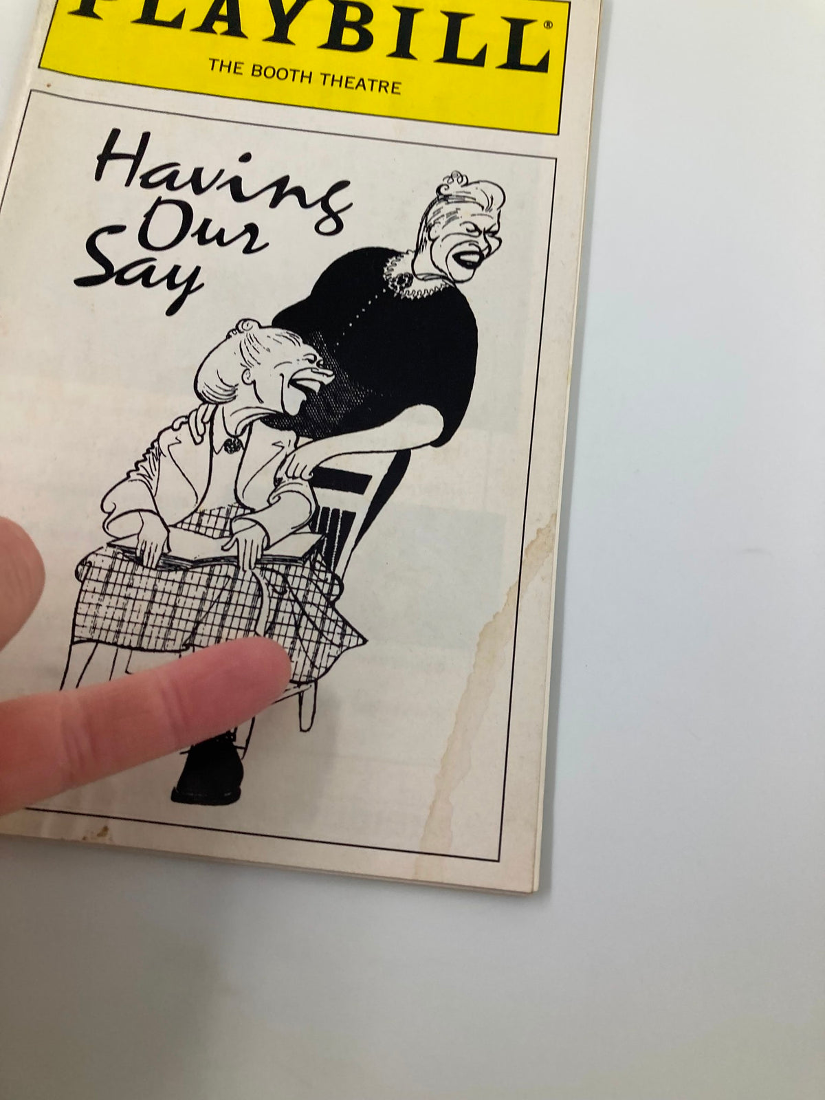 Close-up view of the 1995 Playbill for 'Having Our Say' at the Booth Theatre, showcasing an illustration with a finger pointing to the details, highlighting the theater's collectible significance.