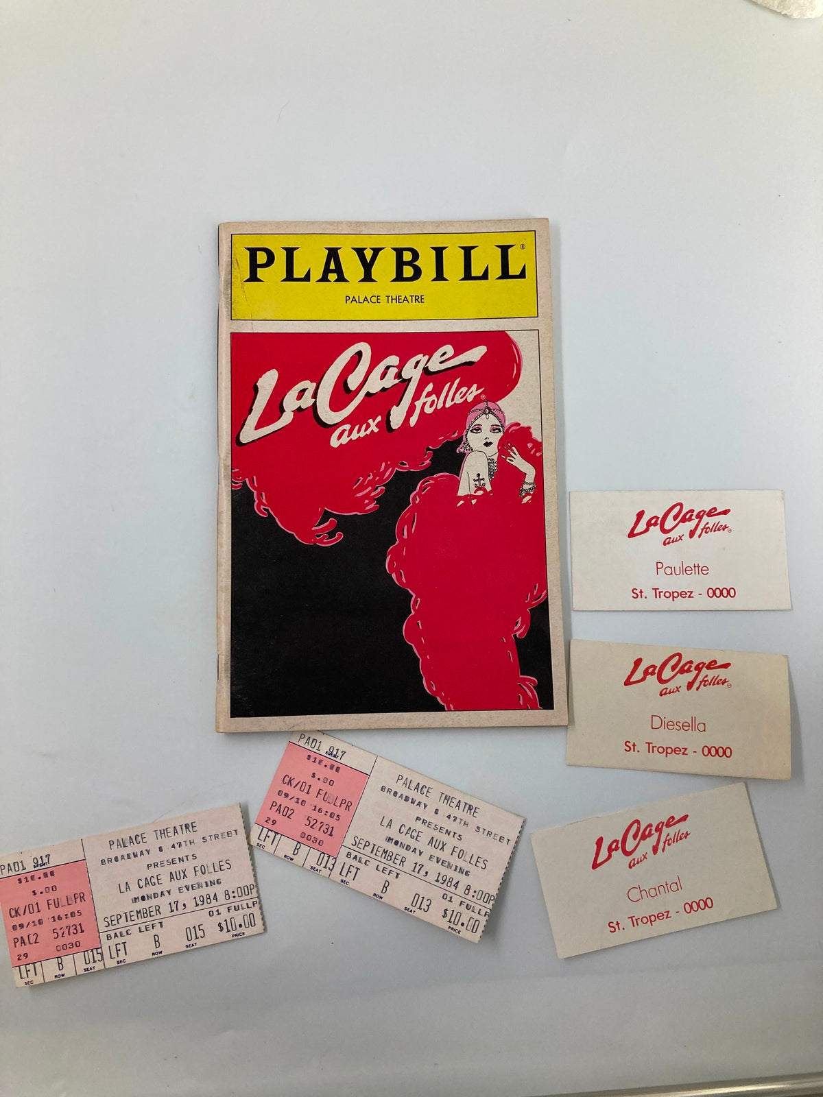 1984 Playbill titled 'La Cage Aux Folles' from The Palace Theatre featuring vibrant cover art with a character in flamboyant attire and ticket stubs for the performance.