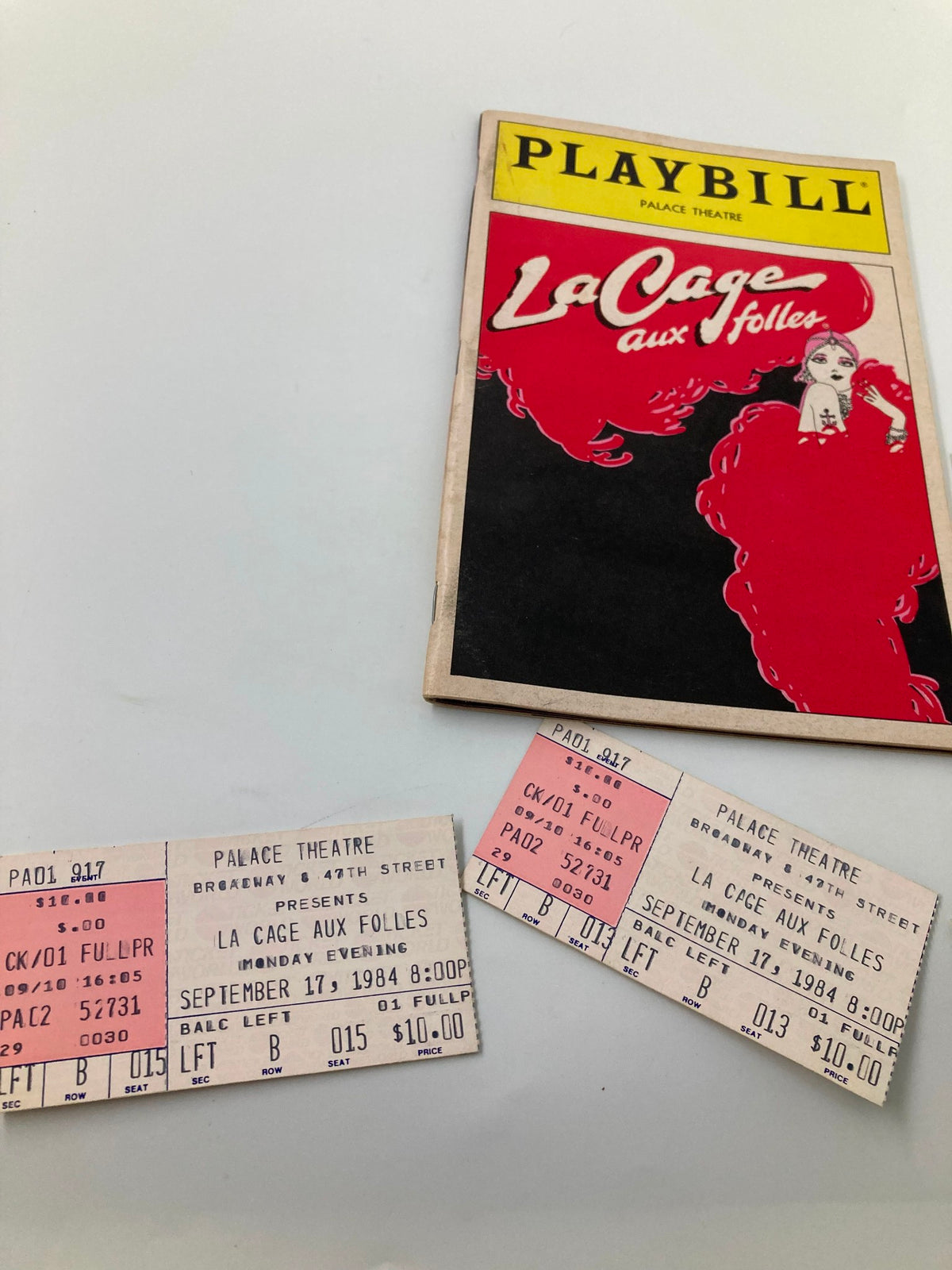 Close-up view of the 1984 Playbill 'La Cage Aux Folles' from The Palace Theatre alongside vintage ticket stubs revealing performance dates and prices.