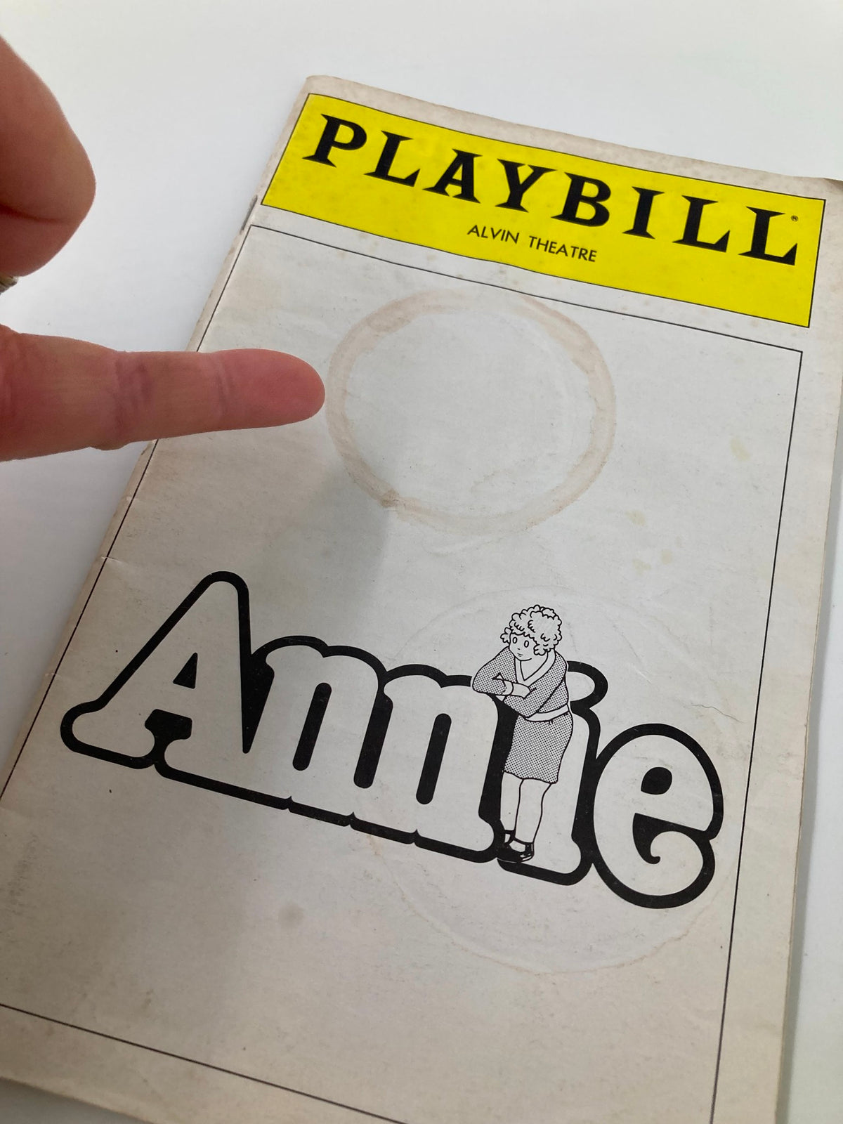 Close-up of the 1980 Playbill for 'Annie' showcasing the cover with a finger pointing at the title.
