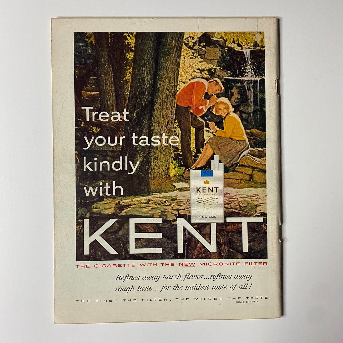 Vintage advertisement for Kent cigarettes, promoting the slogan 'Treat your taste kindly' with a couple enjoying nature, featuring a box of Kent cigarettes prominently.