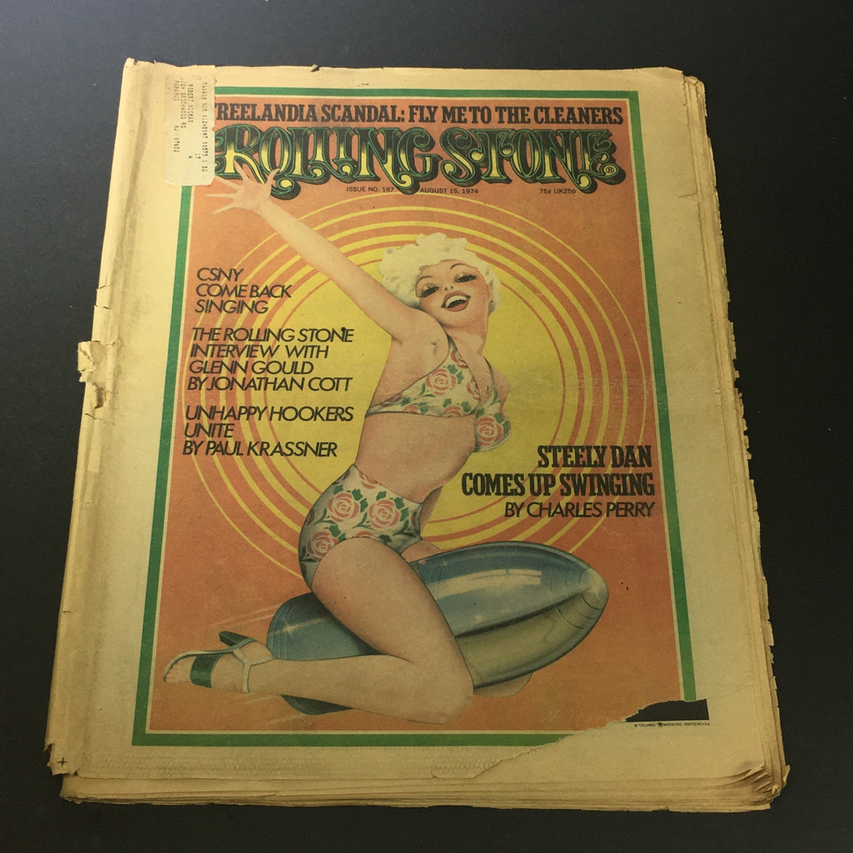 Cover of VTG Rolling Stone Magazine August 15 1974 featuring a vintage illustration of a woman in a swimsuit alongside the headline 'Steely Dan Comes Up Swinging by Charles Perry.' The magazine shows signs of aging with a unique address label.
