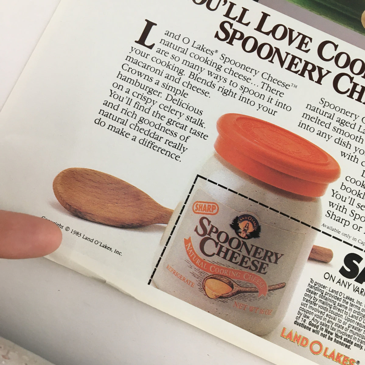Close-up image of the 1983 Sharp Spoonery Cheese Circular Coupon Advertisement, focusing on the jar of Spoonery Cheese and its distinctive orange lid, emphasizing the product's cooking versatility.