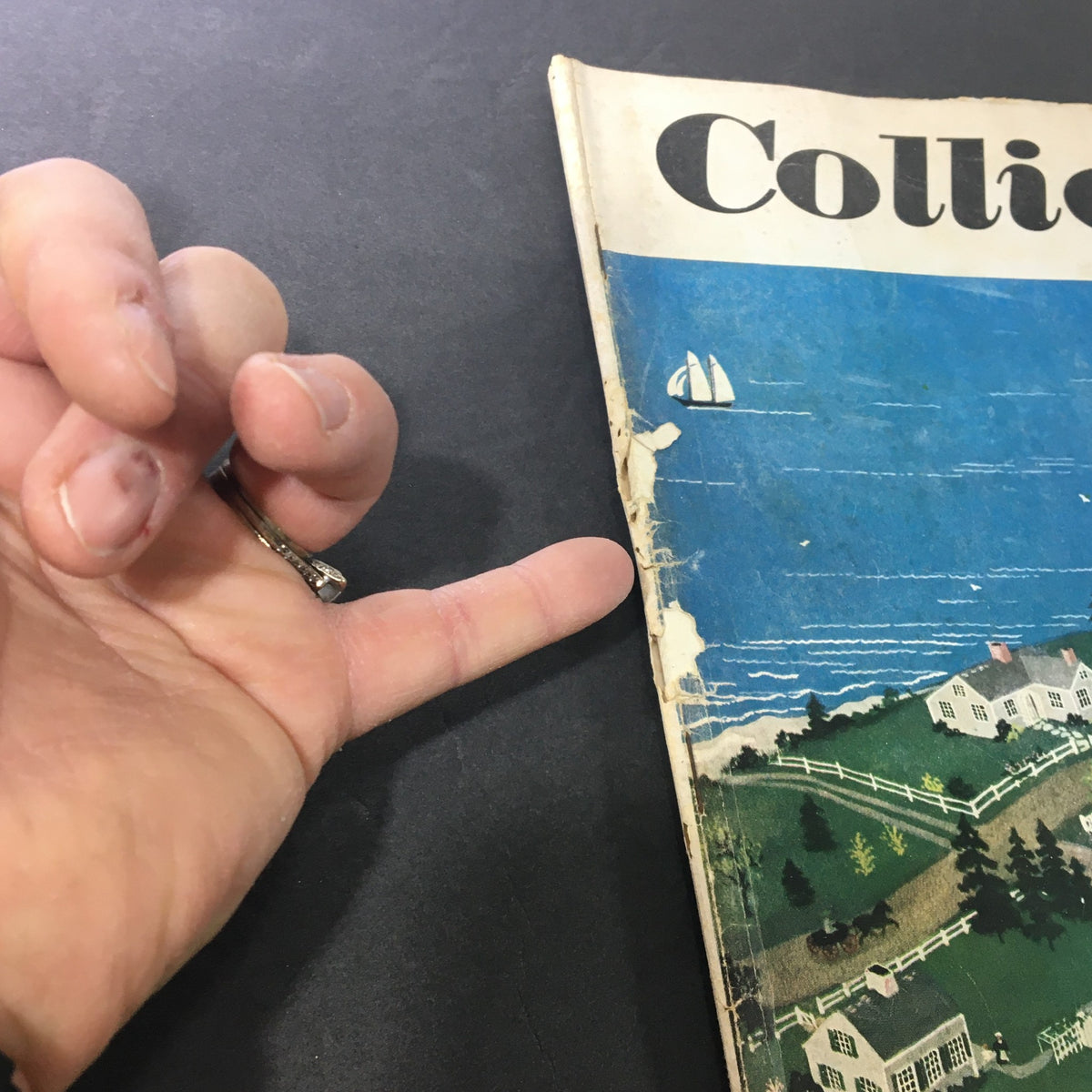 Close-up of the damaged cover of the VTG Collier's Magazine July 16, 1949, showing signs of wear and tear, including a hand pointing at the magazine.