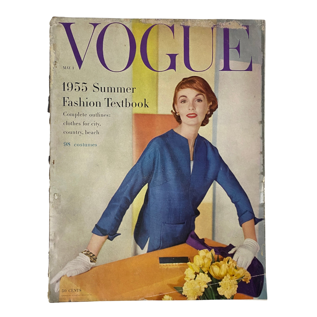 Vogue Magazine May 1, 1955 Summer Fashion Textbook cover featuring a fashionable woman in a blue dress, holding flowers on a table, showcasing mid-century summer fashion.