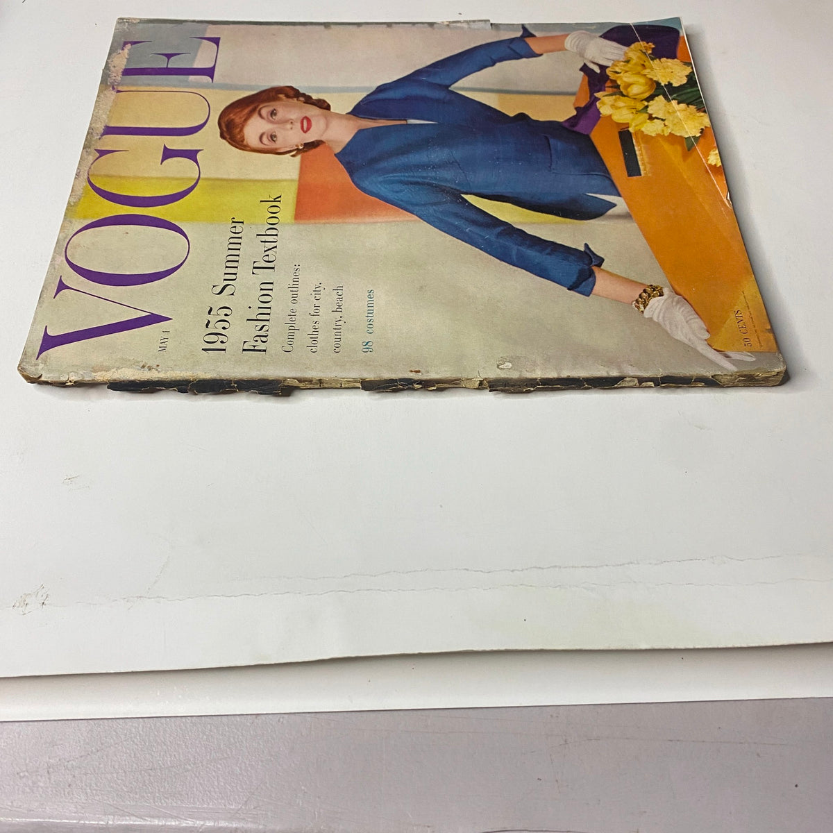 Side view of the Vogue Magazine May 1, 1955 Summer Fashion Textbook, displaying the iconic cover image with a woman in a blue attire and flowers, emphasizing the vintage style.