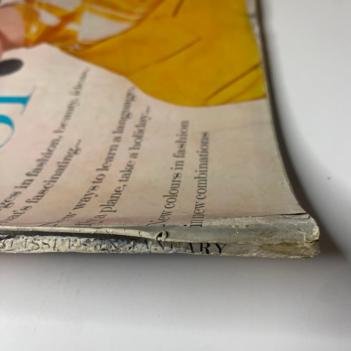 Side view of Vogue Magazine January 1, 1961's spine, showing slight damage and wear, reflecting its vintage condition while maintaining style importance in fashion history.