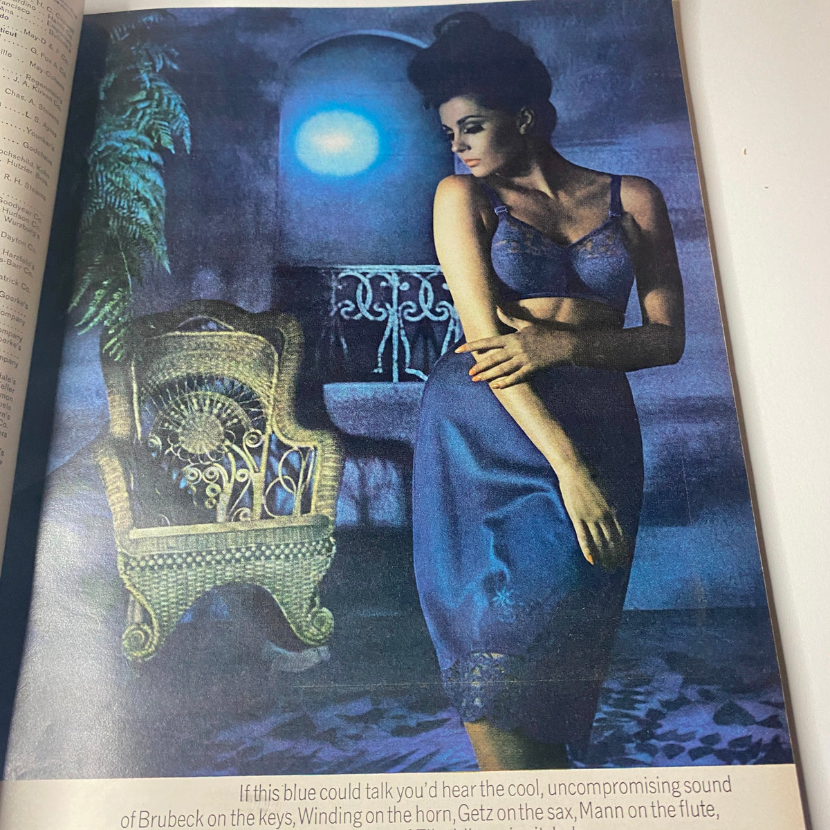 A vintage fashion image from Vogue Magazine October 1, 1964 featuring a model in a blue dress posing elegantly beside a distressed wicker chair, showcasing mid-1960s style and design by Irving Penn.
