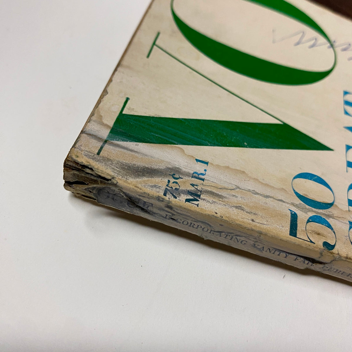 Close-up of the spine of the Vintage Vogue Magazine March 1, 1966, displaying signs of wear and tear, illustrating the magazine's history and vintage characteristics.