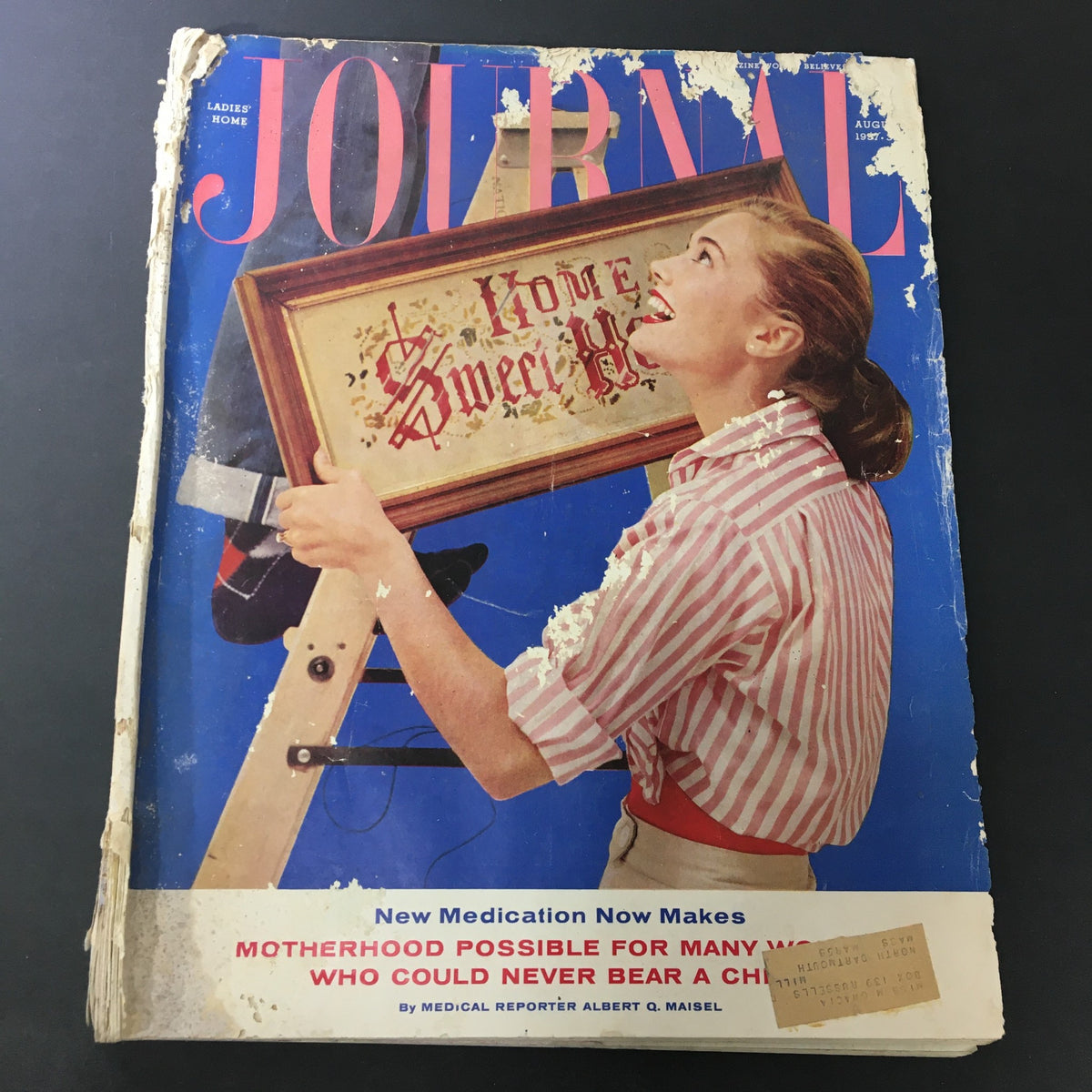 Cover of VTG Journal Magazine August 1957, showcasing a woman holding a framed piece of art with the title 'Home Sweet Home'. This vintage issue highlights nostalgic 1950s themes, with wear and tear indicative of its age.