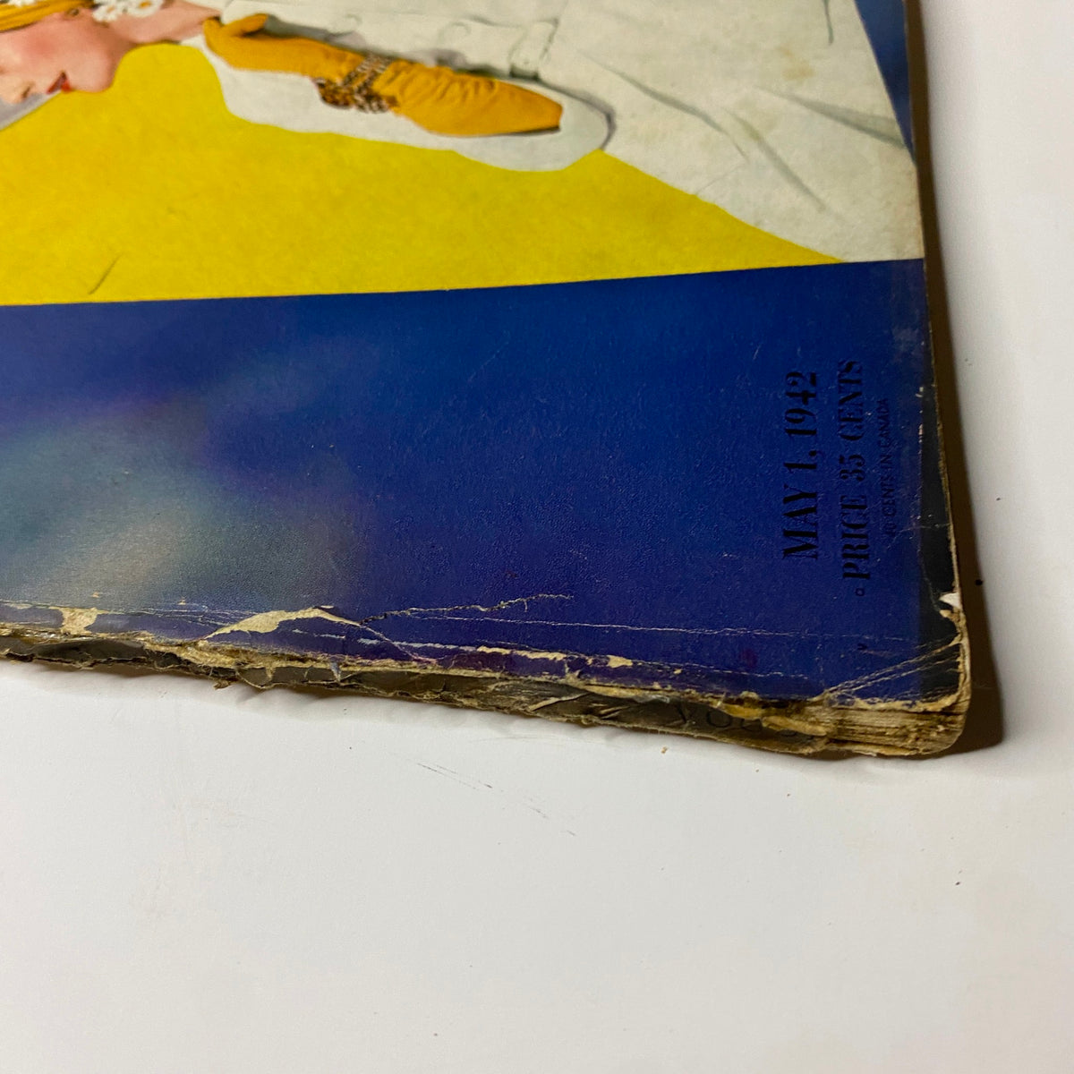 Edge view of the cover of Vogue Magazine May 1, 1942 with visible wear and edge damage, highlighting the magazine's vintage condition.