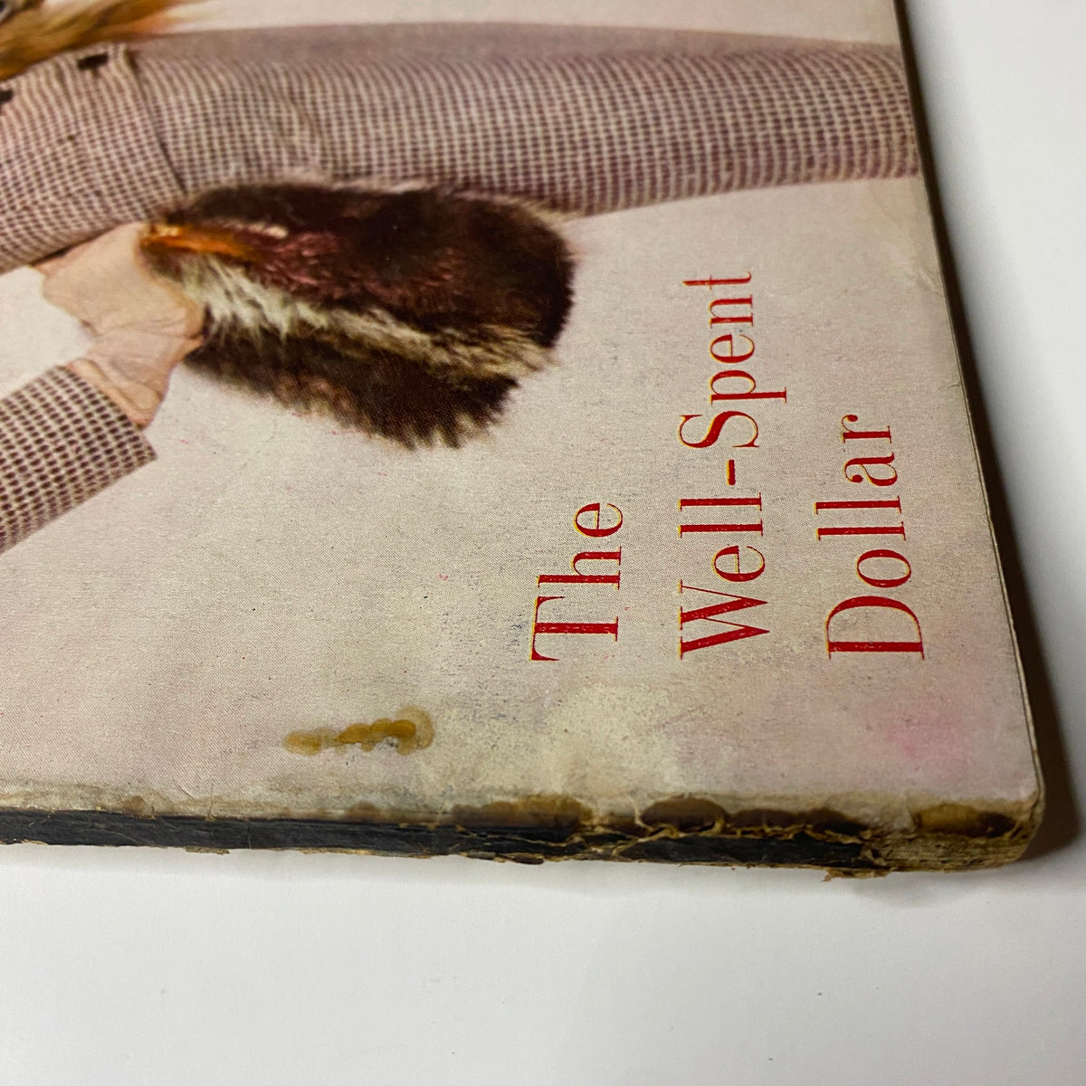 Detail of the bottom corner of Harper's Bazaar Magazine February 1955 cover, featuring the text 'The Well-Spent Dollar,' along with evidence of age-related wear.