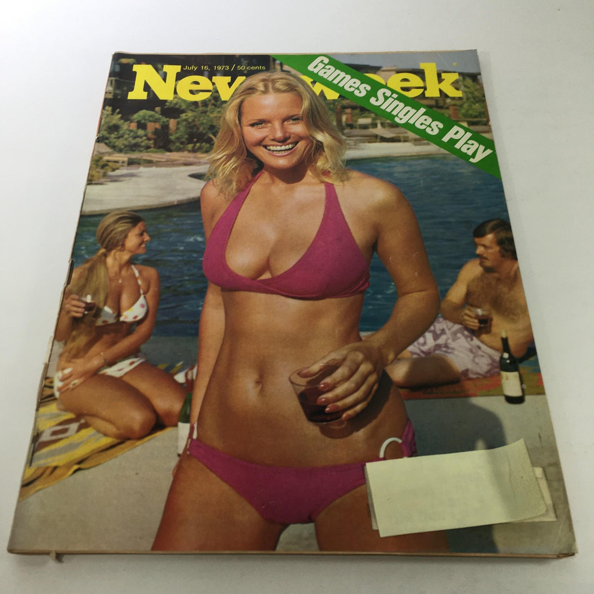 Cover of Newsweek Magazine from July 16, 1973, featuring the title 'Games Singles Play'. The vibrant image showcases a young woman in a pink bikini smiling by a pool, with two other people relaxing in the background, embodying the leisure and culture of the early 1970s.