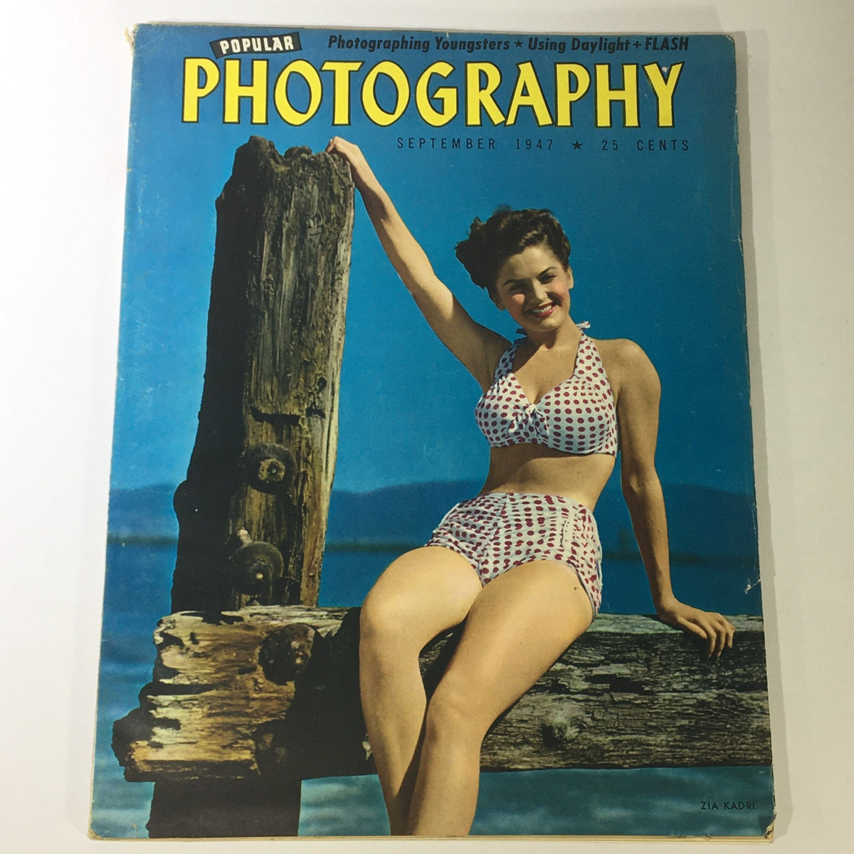 Cover of Popular Photography Magazine September 1947 Vol 21 #3 showcasing a young woman in a polka dot bikini sitting on a wooden post by the beach.