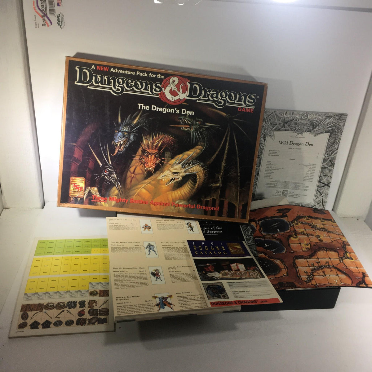TSR Board Game: Dungeons & Dragons Game The Dragon's Den featuring the game box, adventure pack, game board, and accompanying materials laid out on display.