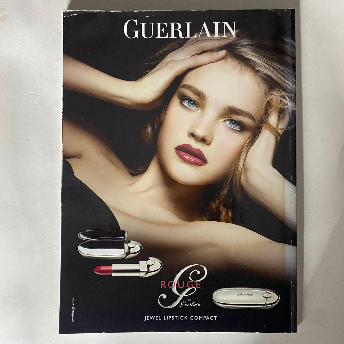Guerlain advertisement featuring a model with stunning makeup, promoting the Rouge de Guerlain Jewel Lipstick Compact.