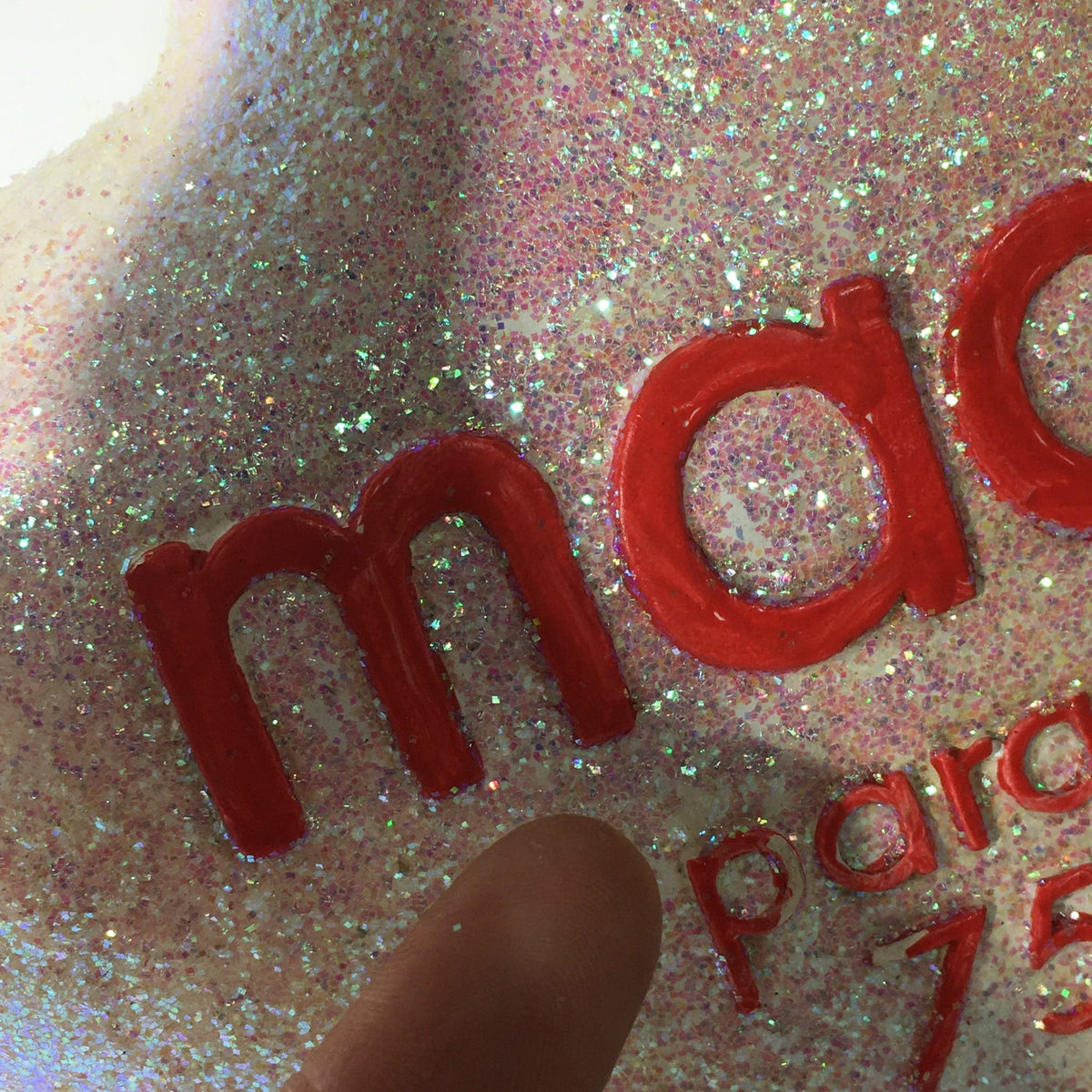 Detailed view of the letter 'm' on the Macy's Thanksgiving Day Parade 75th Anniversary Collectible star ornament, showcasing the vibrant red color among festive glitter.