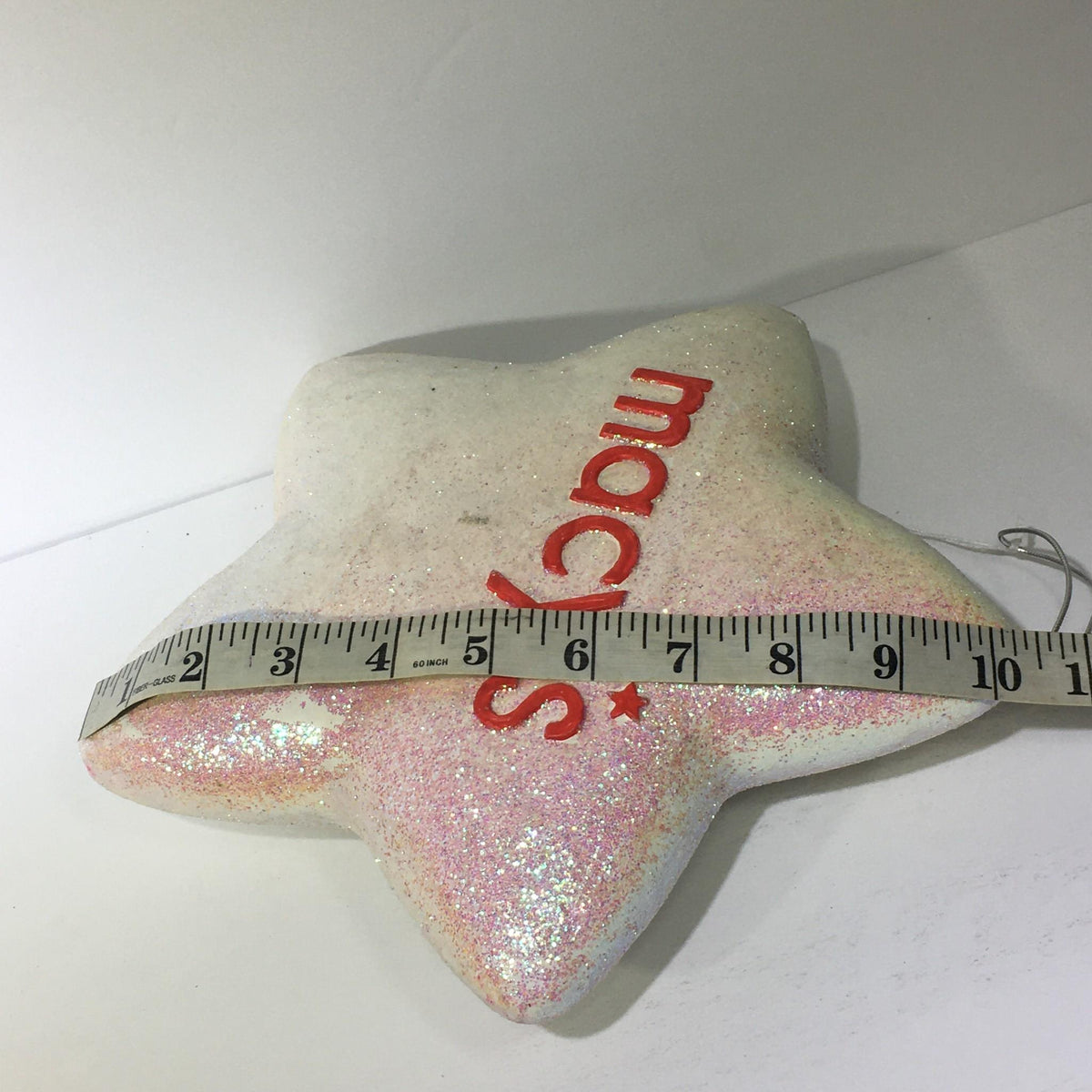 Measuring the glittery star ornament from Macy's Thanksgiving Day Parade 75th Anniversary Collectible, showing its dimensions clearly.