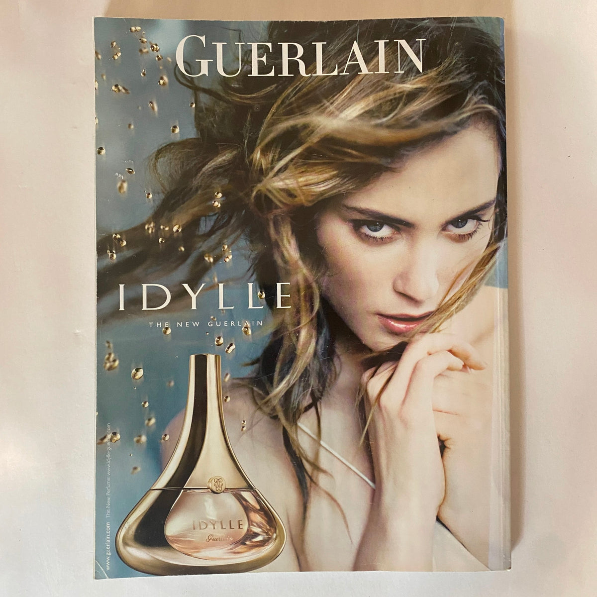 The cover of Harper's Bazaar UK Magazine December 2009 featuring the Guerlain Idylle fragrance ad, showcasing a model with flowing hair and a bottle of Idylle perfume, emphasizing timeless elegance and beauty.