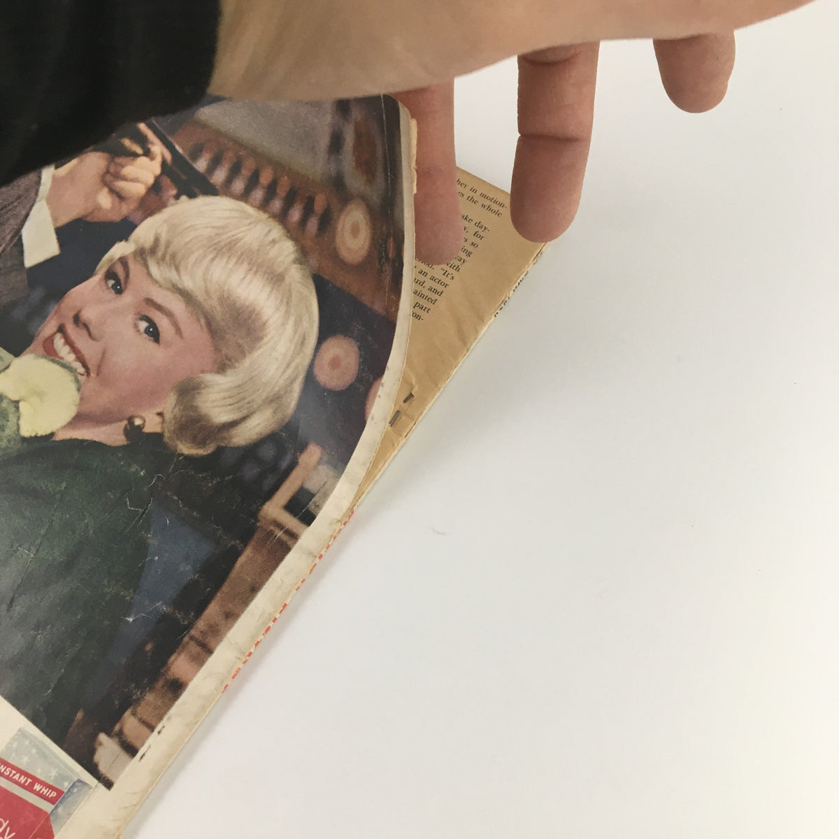 Hand flipping through the pages of a vintage magazine with an advertisement on display, showcasing content from VTG Motion Picture Magazine April 1959 Dick Clark and Family Cover.