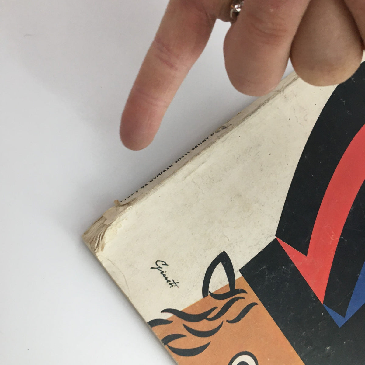 Another angle of the VTG Holiday Magazine April 1958 displaying the bottom edge with damage, with a hand pointing at the front cover design and details.