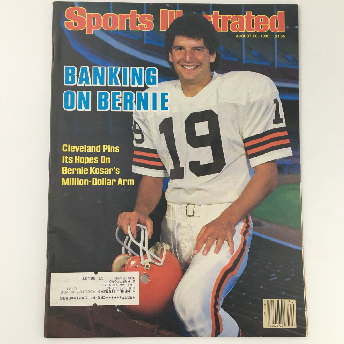 Sports Illustrated Magazine from August 26, 1985, featuring the iconic Bernie Kosar on the cover with the headline 'Banking on Bernie.' The magazine highlights Bernie Kosar, wearing Cleveland Browns gear, as he poses with a football helmet on a sports field.