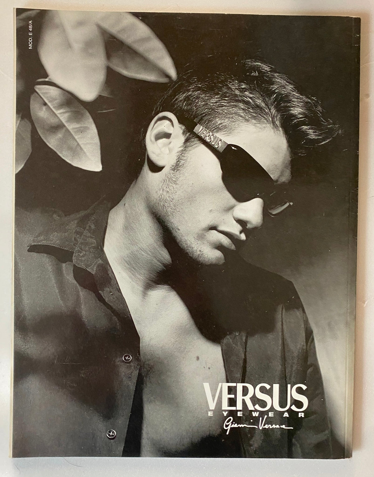 Italia Magazine 1998 advertisement for Versus eyewear, displaying a male model wearing sunglasses against a black and white backdrop. This striking image highlights fashion trends from the late 90s.