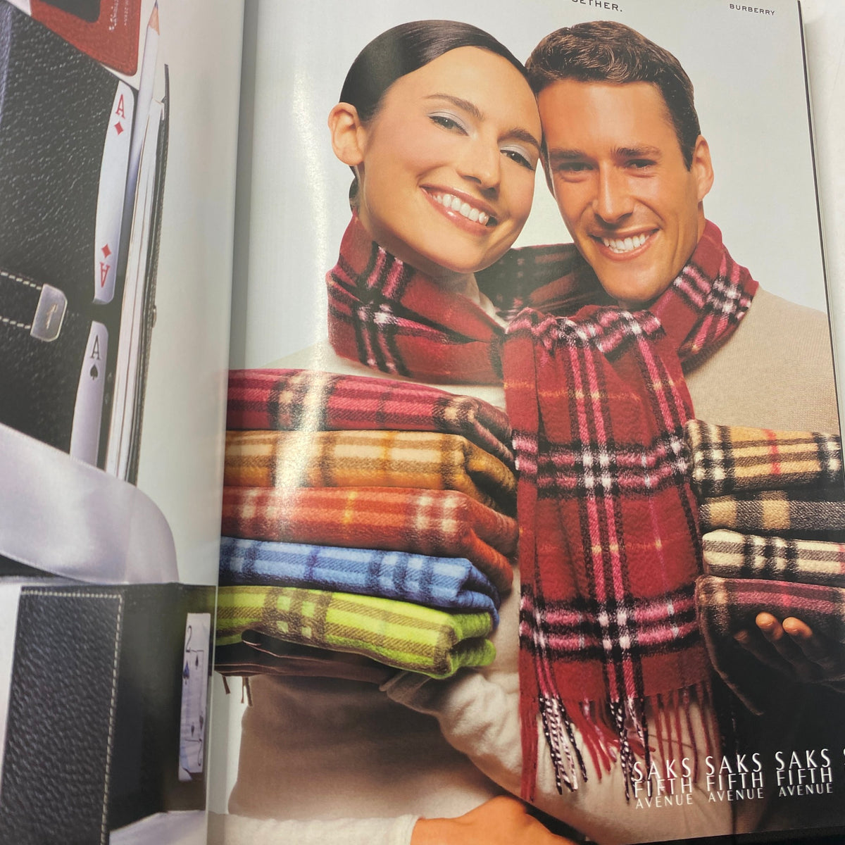 Saks Fifth Avenue advertisement featuring a smiling couple wrapped in colorful scarves, showcasing winter fashion in a fashionable layout.