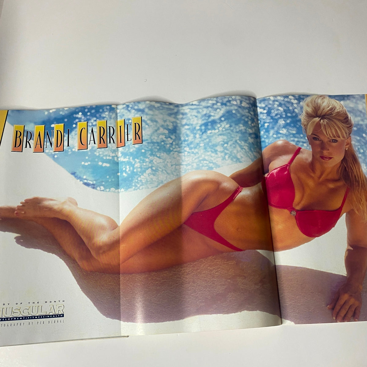 Fold-out poster of Brandi Carrier from Muscular Development Magazine November 1996, showcasing her in a red bikini by the pool.