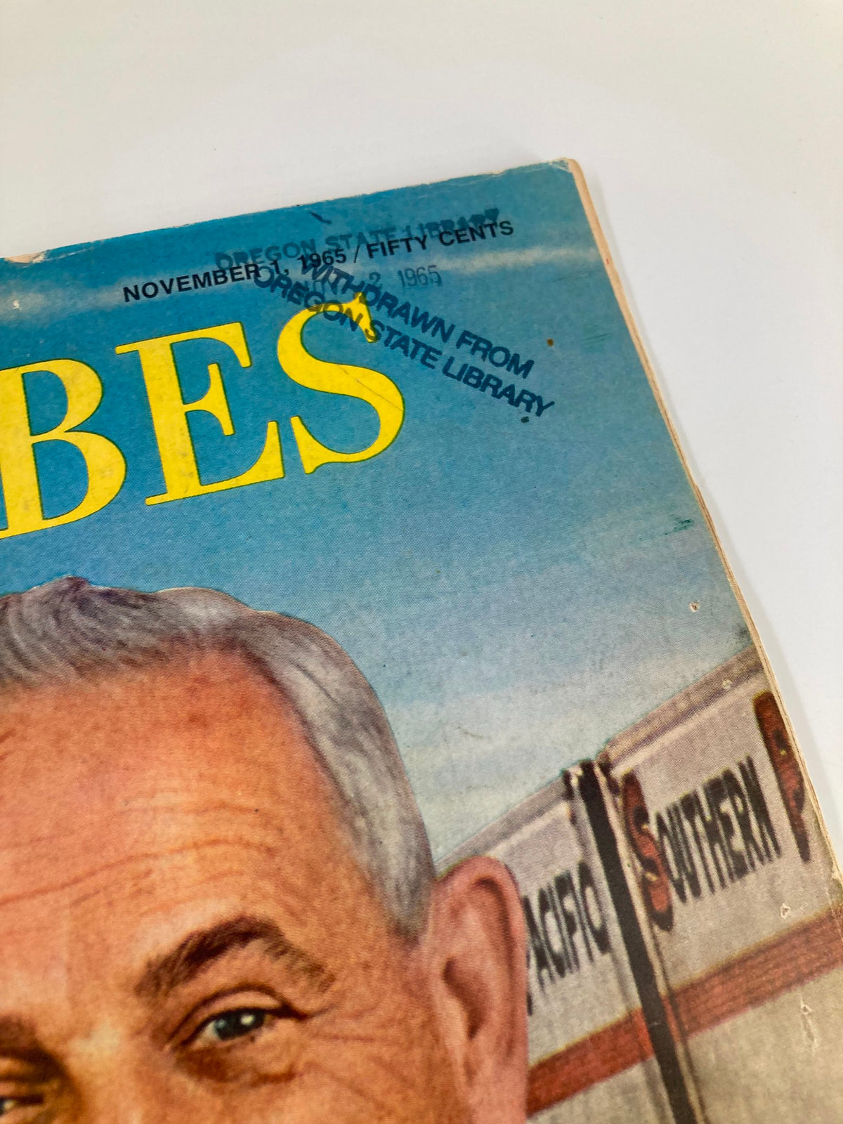 Close-up of the cover of Forbes Magazine dated November 1, 1965, featuring a stamped mark indicating it was withdrawn from Oregon State Library. Highlights the magazine's historical significance regarding Southern Pacific's Donald Russell.