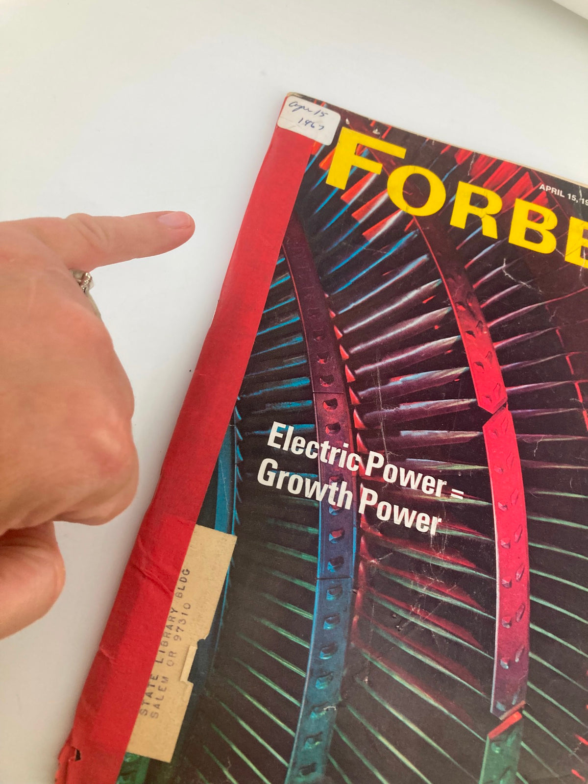 Close-up of the cover of VTG Forbes Magazine April 15, 1967, showing the title and part of the magazine's graphics with a hand pointing at the cover.