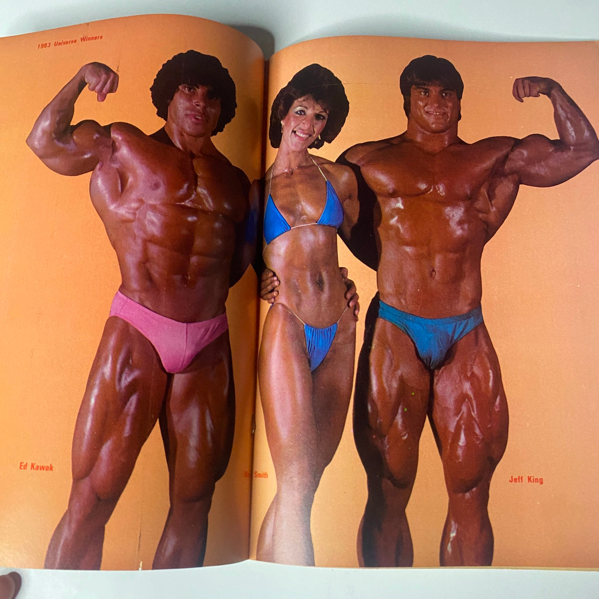 Centerfold image from Muscle & Bodybuilder Magazine May 1984 showing bodybuilders Ed Kawak and Jeff King alongside a female competitor.