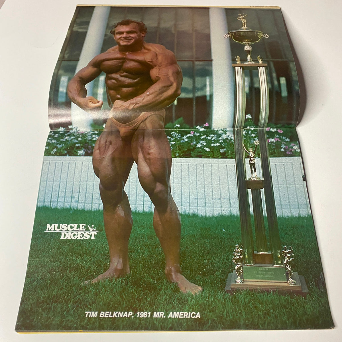 Tim Belknap showcasing his physique in the December 1981 issue of Muscle Digest Magazine, Volume 5, Number 5, next to his trophy from Mr. America.