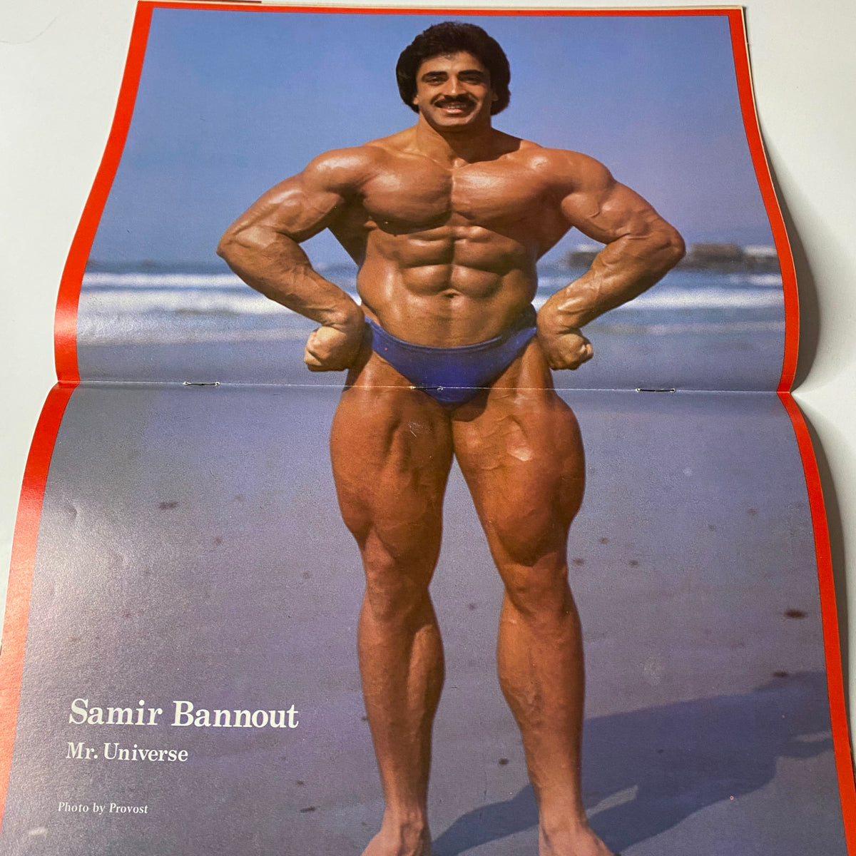 Centerfold of Muscle Training Illustrated October 1980, Issue No. 87, showcasing Samir Bannout, Mr. Universe, posing on the beach in a blue swimsuit, emphasizing his muscular physique.