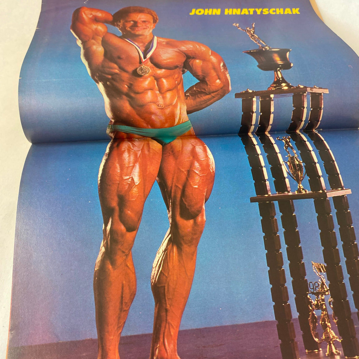 Centerfold spread in Muscle Up Magazine Fall 1985 featuring bodybuilder John Hnatyschak posing with a trophy, showcasing his muscular physique.