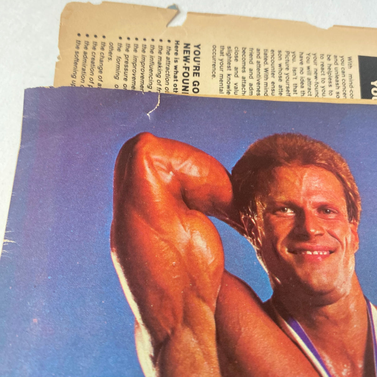 Detail close-up shot in Muscle Up Magazine Fall 1985 of John Hnatyschak flexing with a medal around his neck, highlighting his strength and conditioning.