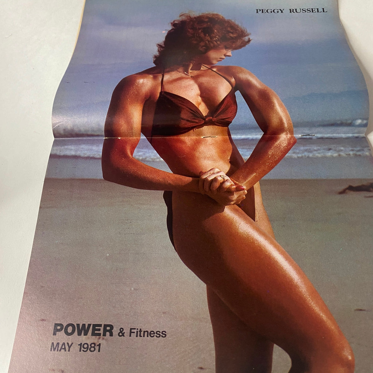 Centerfold of Power & Fitness for Everybody May 1981 showcasing Peggy Russell, emphasizing her physique on the beach.